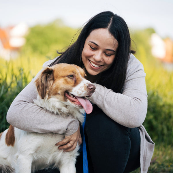 Smiling woman hugging brown and white dog outdoors during travel adventures