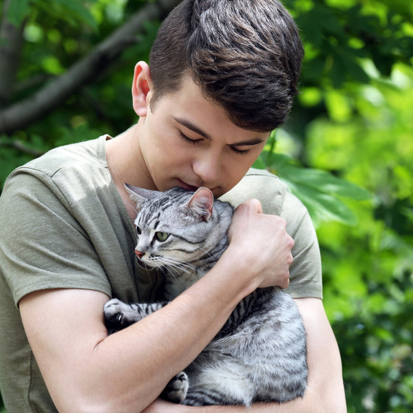 Young man gently hugging his adorable tabby cat outside in nature